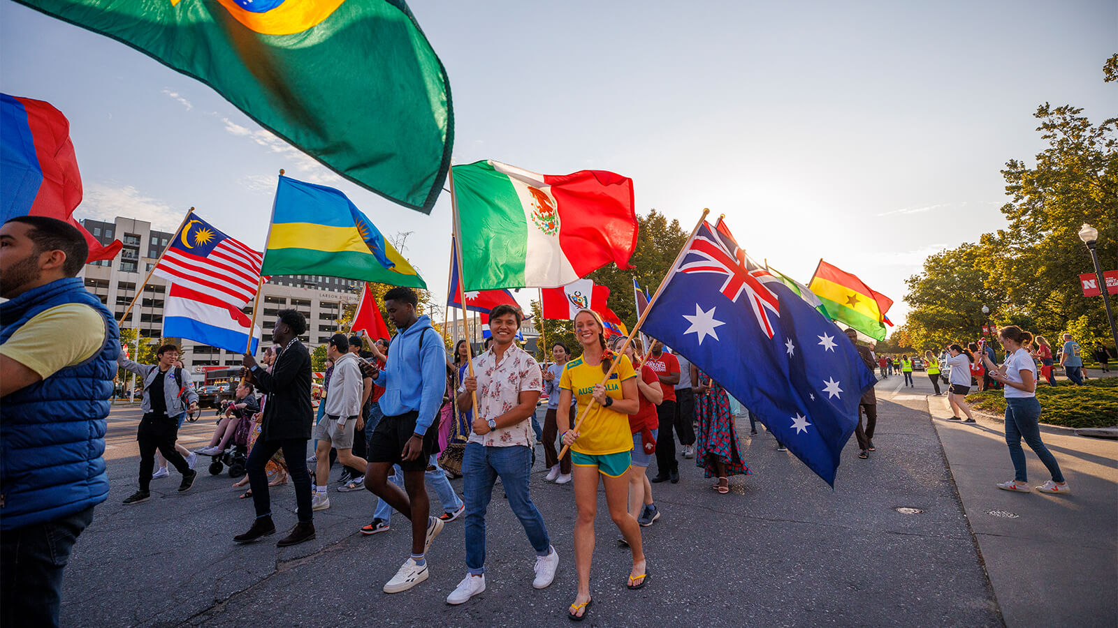 A parade of students waving flags of various countries march in the street on a wonderful sunny day.