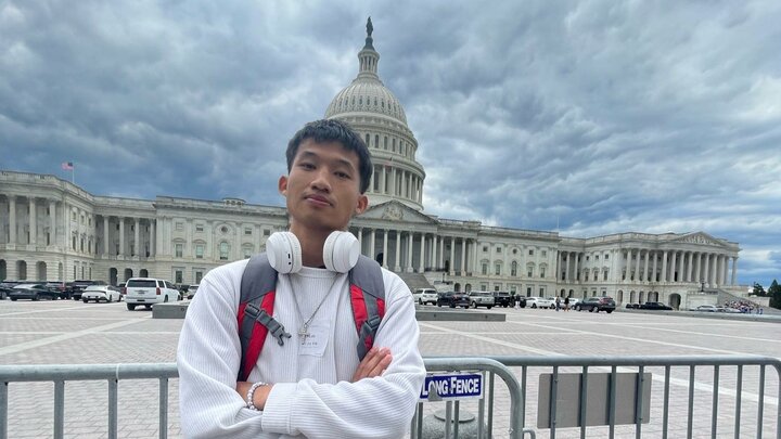 Eh Ta Taw in front of the U.S. Capitol dome under cloudy skies, wearing headphones and a backpack.