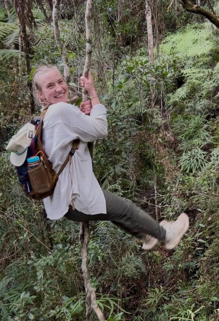 Person smiling while swinging on a vine in a lush forest.